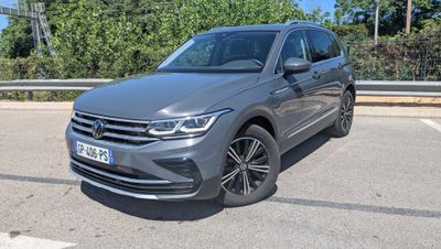 une Volkswagen Tiguan grise garée sur un parking près des arbres
