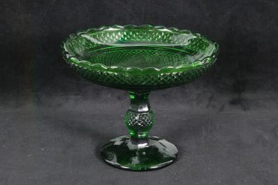 un bol en verre vert posé sur un socle, sur fond noir
