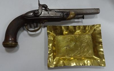 un vieux pistolet et une assiette en or posée sur une table blanche