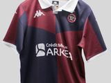 La chemise est bordeaux et bleue, avec un col blanc.