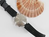 a watch sitting next to a shell on a white surface