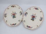 two plates with floral designs on them sitting on a white surface