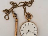 a gold pocket watch and a gold chain on a white surface
