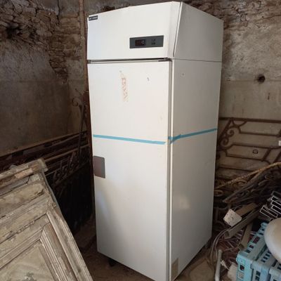 un réfrigérateur blanc dans une pièce sale, avec une bande bleue sur la porte