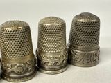 three antique thimbles are lined up on a white surface