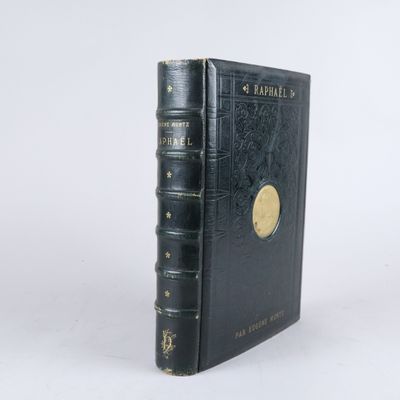 un vieux livre noir aux tranches dorées posé sur une surface blanche