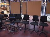 several black office chairs in a warehouse with a screen in the background