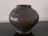 a black vase sitting on a table with a white wall in the background