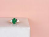 a close up of a green emerald and diamond ring on a pink background