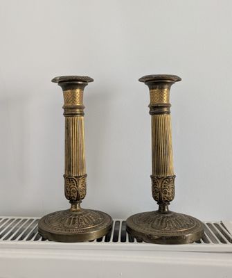 pair of antique brass candlesticks on a shelf in front of a white wall