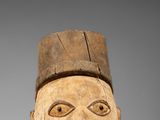 un masque en bois avec un grand visage et un chapeau sur la tête