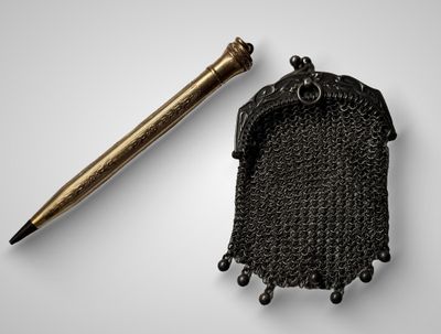 une cotte de mailles métallique et un stylo posés sur une surface blanche