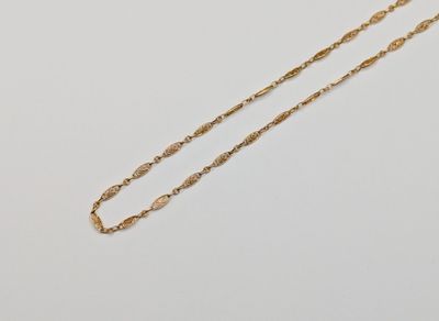un collier en or muni d'une longue chaîne, posé sur une surface blanche