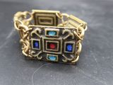 un gros plan d'une bague en or sertie de pierres bleues, rouges et vertes