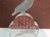 a bird sitting on top of a birdcage on a table