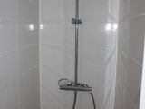 a shower head in the corner of a white tiled bathroom