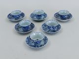 six tasses à thé et soucoupes bleues et blanches posées sur une surface blanche