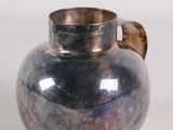 a silver vase with a brown handle on a white surface