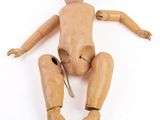 une poupée en bois assise sur une surface blanche, tenant une paire de ciseaux