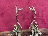 une paire de figurines anciennes en laiton posées sur une table en bois, sur un fond rose