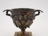 a bronze vase that is on a wooden stand