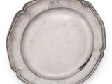 une assiette ancienne en argent sur fond blanc, ornée d’un blason sur le bord