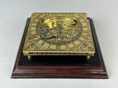 an antique brass clock on a wooden base on a white background