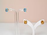 paire de boucles d'oreilles en cristal de topaze bleue et de topaze jaune, posées sur un socle blanc
