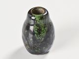 a black vase with green speckles sitting on a white surface