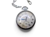 a silver pocket watch on a chain on a white surface