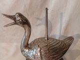 un canard en argent posé sur un socle en bois, avec un cure-dent dans le bec