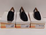 trois paires de chaussures noires posées sur des cartons, sur une surface blanche