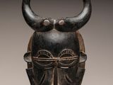a close up of a wooden mask with horns on a stand