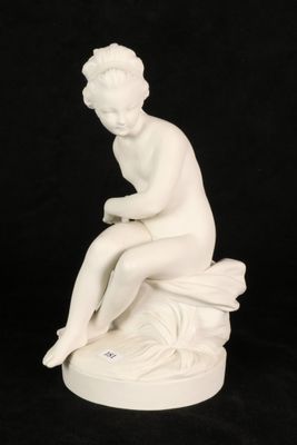 a white statue of a woman sitting on top of a rock