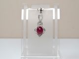 necklace with a red stone in a clear display case on a white surface