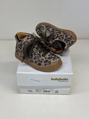 des chaussures de bébé à imprimé léopard posées sur une boîte, sur une surface blanche