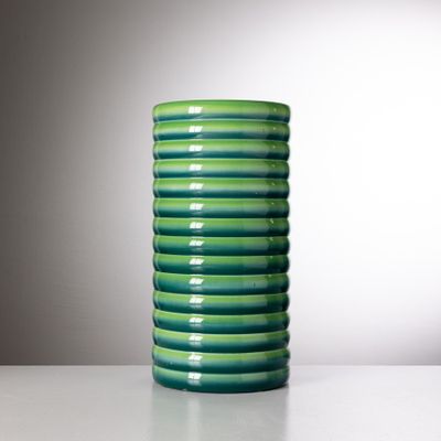 un vase vert posé sur une table avec un mur blanc en arrière-plan