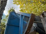 une benne bleue posée contre le mur d'un immeuble, à côté d'un arbre