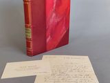 un vieux livre rouge posé sur une table, à côté d'une feuille de papier