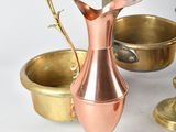 a copper pitcher sitting on top of a table next to other brass dishes