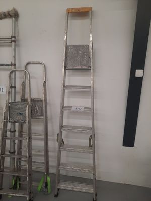 Plusieurs échelles sont alignées contre un mur blanc dans une pièce.