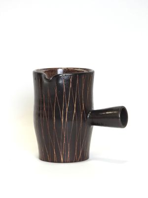 a black cup with a brown handle on a white surface