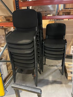 Quatre chaises noires sont empilées sur un chariot dans un entrepôt