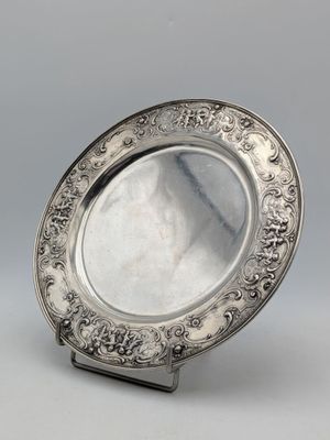 une assiette en argent posée sur un support, sur une surface grise
