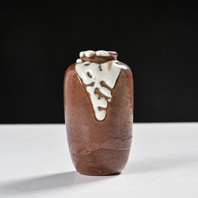 un vase marron posé sur une table blanche, sur fond noir