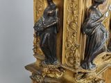 a gold clock with two statues on top of it