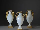 trois vases blancs aux anses dorées posés sur une table