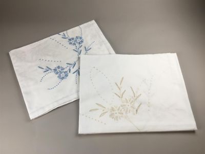 two white napkins with blue flowers on them sitting next to each other