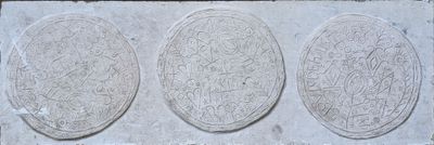 three oval stone plaques with designs on them on a stone wall