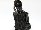 statue of a woman sitting on a tree stump with a hat on her head